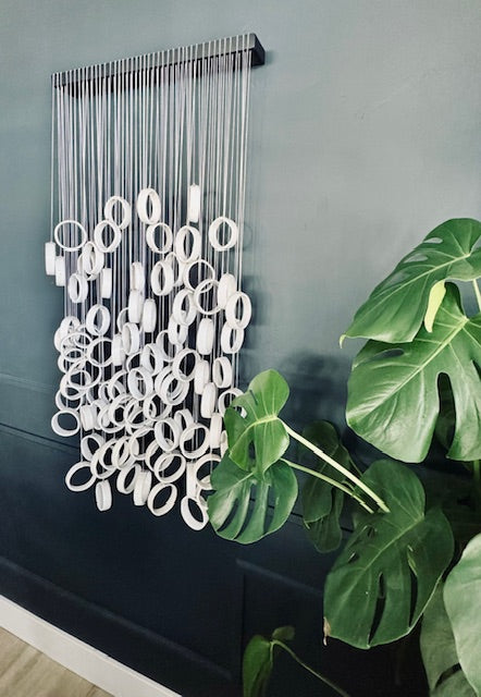 Decorative wall art with white circular shapes on a gray wall, next to a green plant.