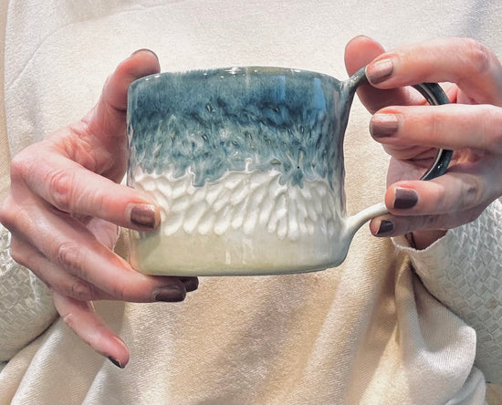 Person holding a ceramic mug with a gradient design, filled with a white glaze.