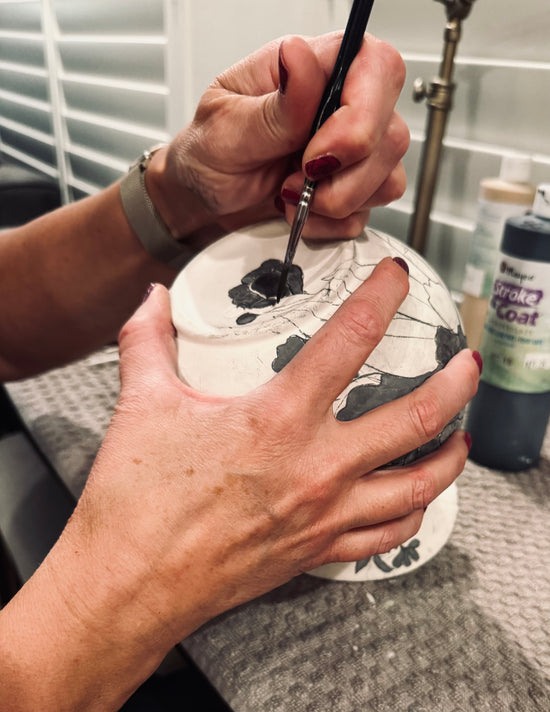 Person painting a ceramic piece with a brush in a kitchen setting