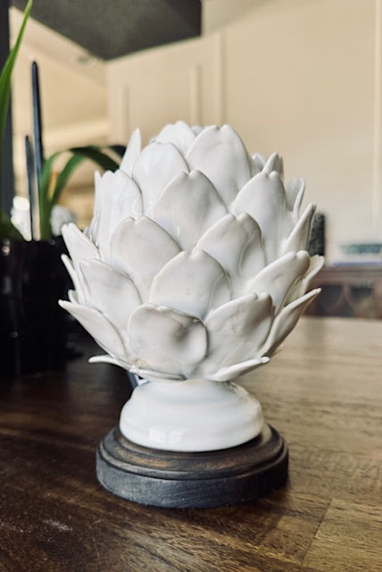 White ceramic artichoke sculpture on a wooden base in a kitchen setting