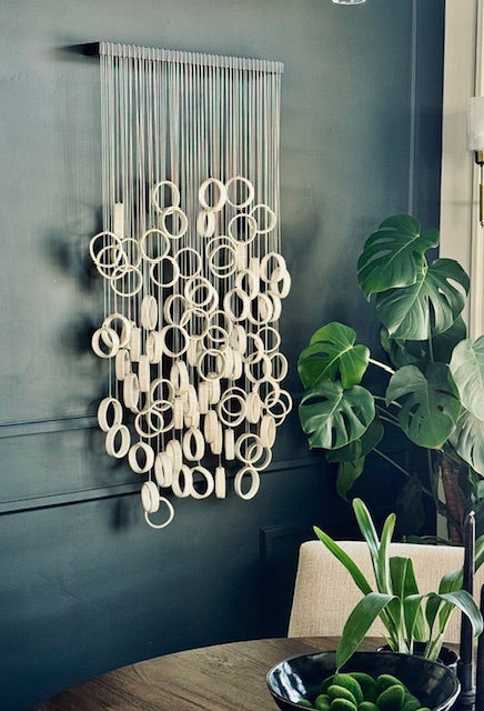 Decorative wall hanging with circular patterns on a dark wall, next to a plant.