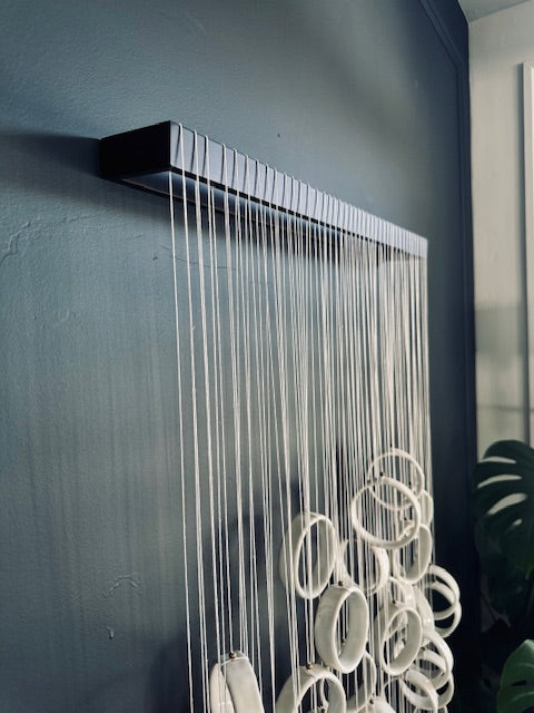 Wall-mounted shower head with hanging ceramic rings against a dark wall.