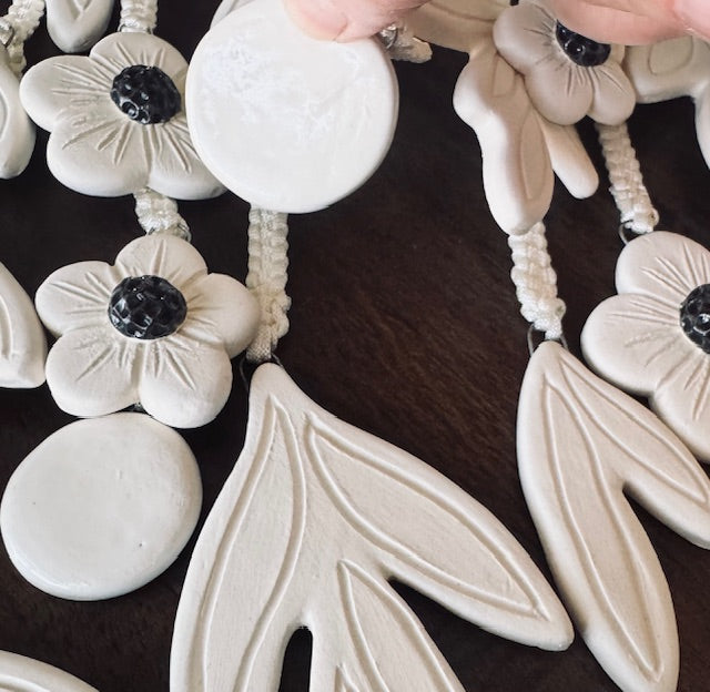 Close-up of a ceramic tiles with white floral and leaf-shaped beads on a dark surface