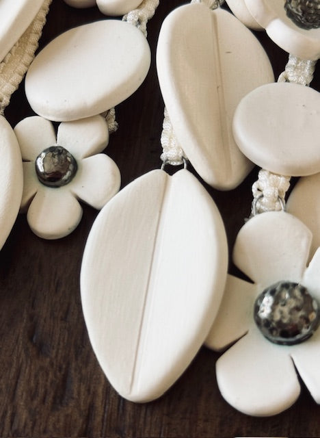 Close-up of a wall hanging tiles with white floral pendants and gray beads on a dark surface