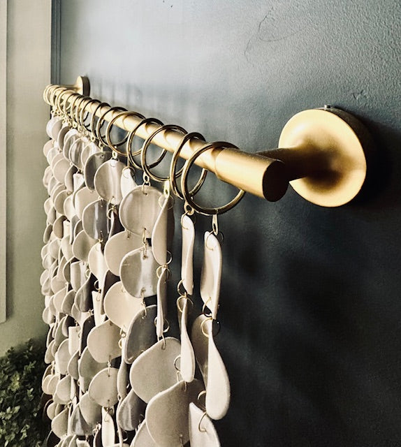 Gold curtain rod with white decorative wall hanging against a dark wall